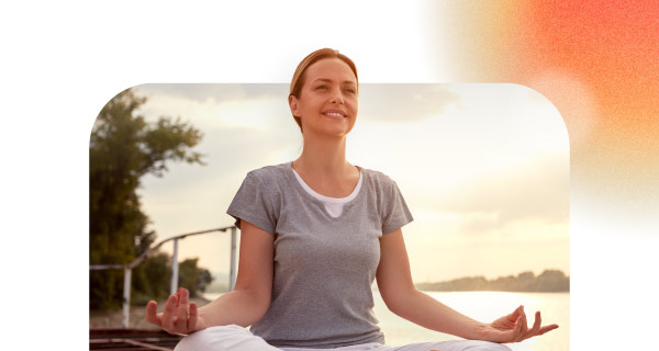 A woman with her hands on her knees, meditating on the beach.